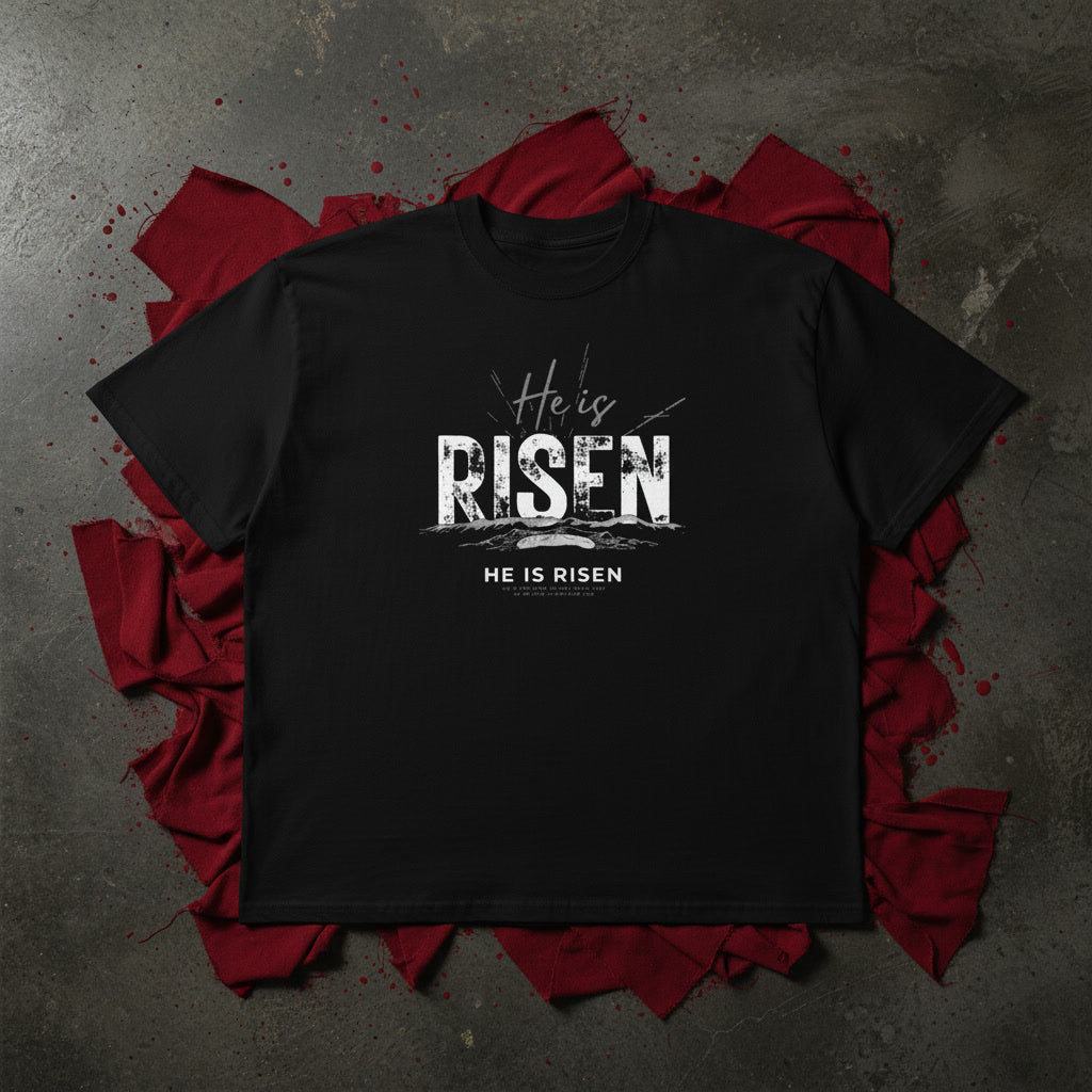 He Is Risen oversized tee in black flat lay — distressed RISEN type over the empty grave, Christian streetwear