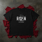 He Is Risen oversized tee in black flat lay — distressed RISEN type over the empty grave, Christian streetwear